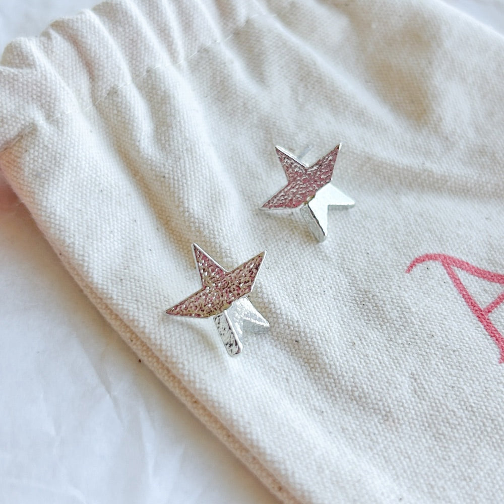 Aros de Plata Barcelona con diseño de estrella y textura brillante, fabricados en acero quirúrgico bañado en plata 925, exhibidos sobre bolsa de tela Altapinta.