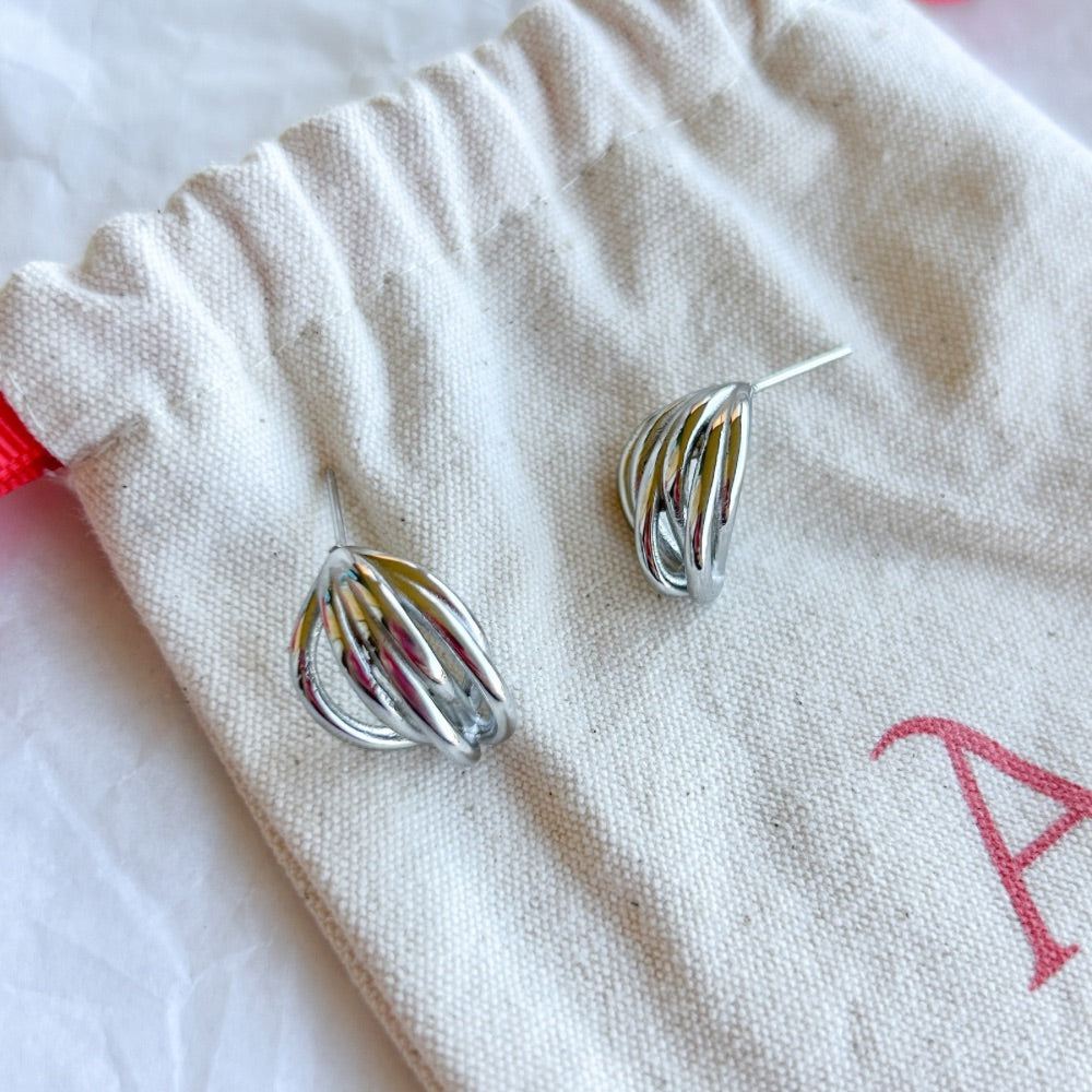 Aros de Plata Basilea con diseño entrelazado en acabado brillante, fabricados en acero quirúrgico bañado en plata 925, exhibidos sobre bolsa de tela Altapinta.