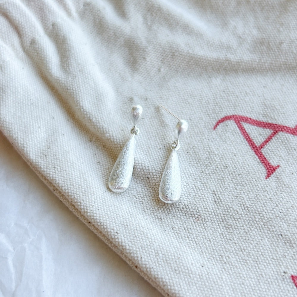 Aros de Plata Braga con diseño de gota alargada y acabado satinado, fabricados en acero quirúrgico bañado en plata 925, sobre bolsa de tela Altapinta.