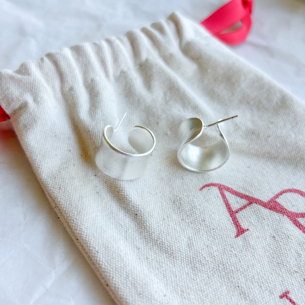 Aros de Plata Estocolmo con diseño curvo y acabado mate en plata 925, exhibidos sobre una bolsa de tela Altapinta.