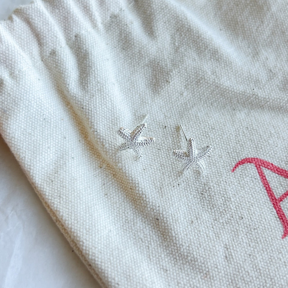 Aros de Plata Gante con diseño de estrella de mar y textura detallada en plata 925, exhibidos sobre una bolsa de tela Altapinta.