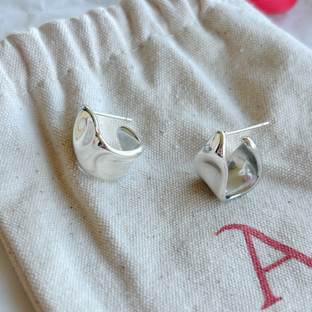 Aros de Plata Londres con diseño ondulado en acabado pulido, exhibidos sobre una bolsa de tela Altapinta.