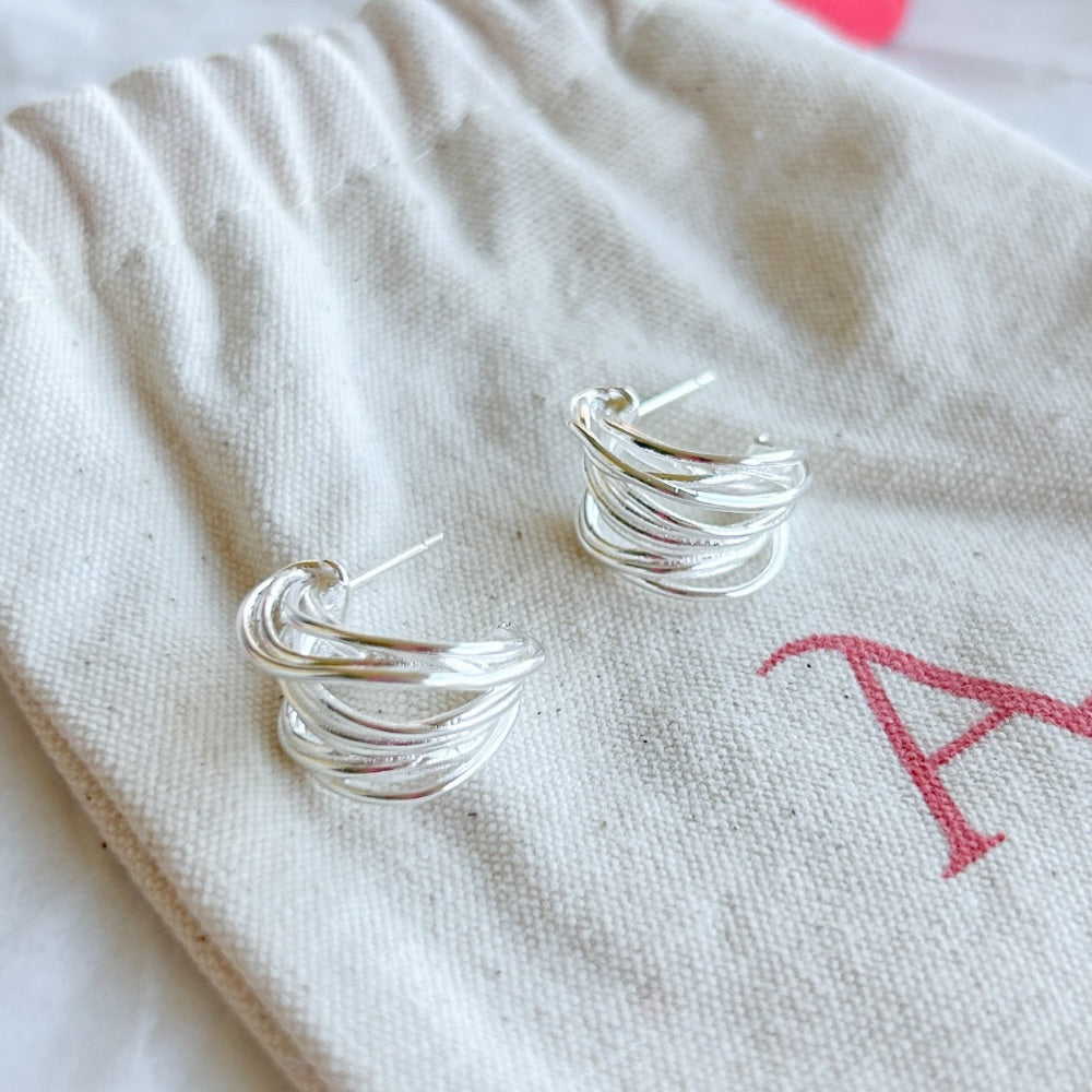 Aros de Plata Madrid con diseño entrelazado y acabado pulido, exhibidos sobre una bolsa de tela Altapinta.