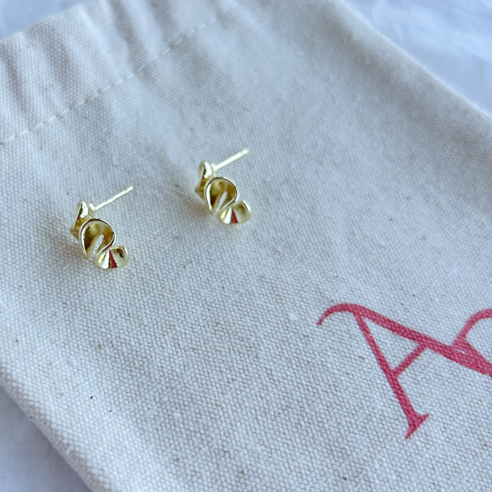 Aros Manchester en baño de oro con forma moderna sobre bolsa de tela.