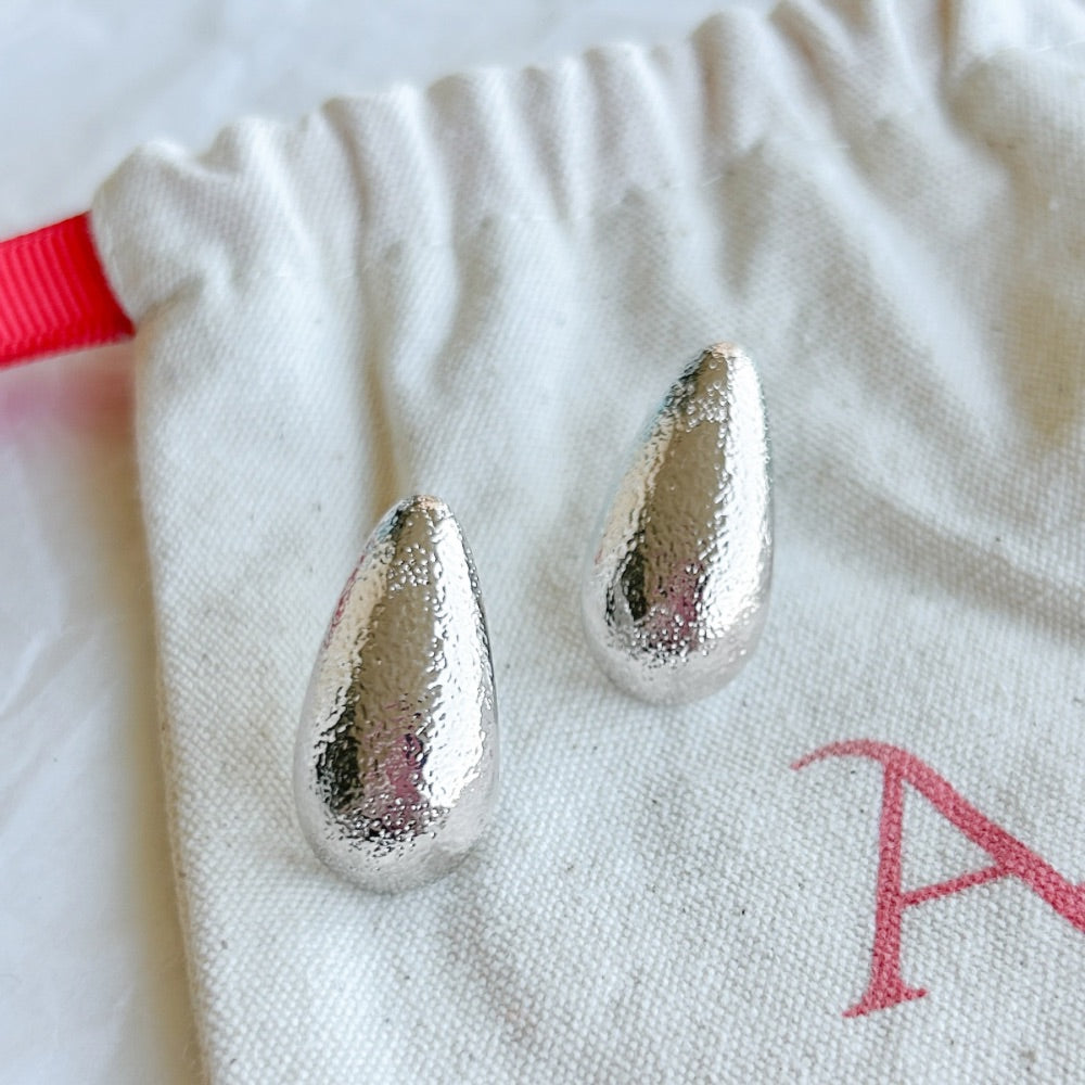 Aros de plata Nápoles con textura martillada en forma de gota sobre bolsa de tela.