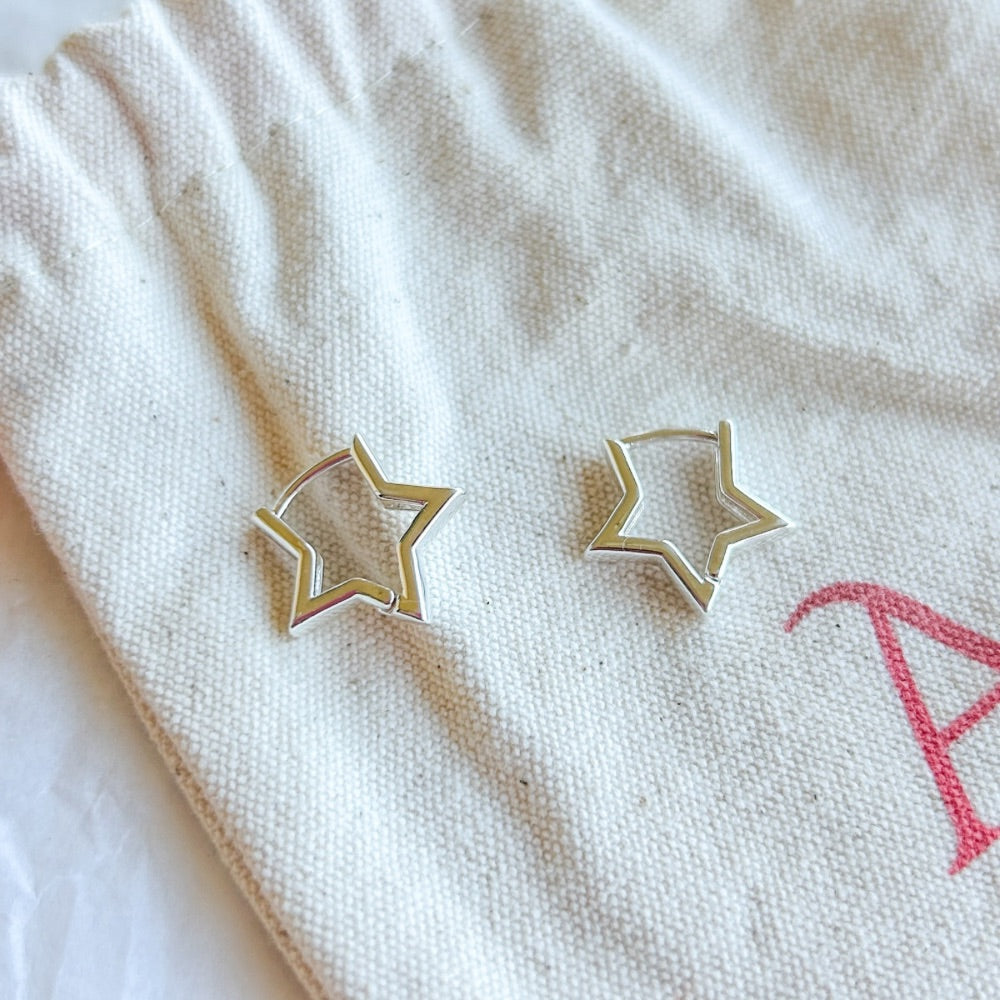 Aros de plata Oporto con diseño de estrella geométrica sobre bolsa de tela.