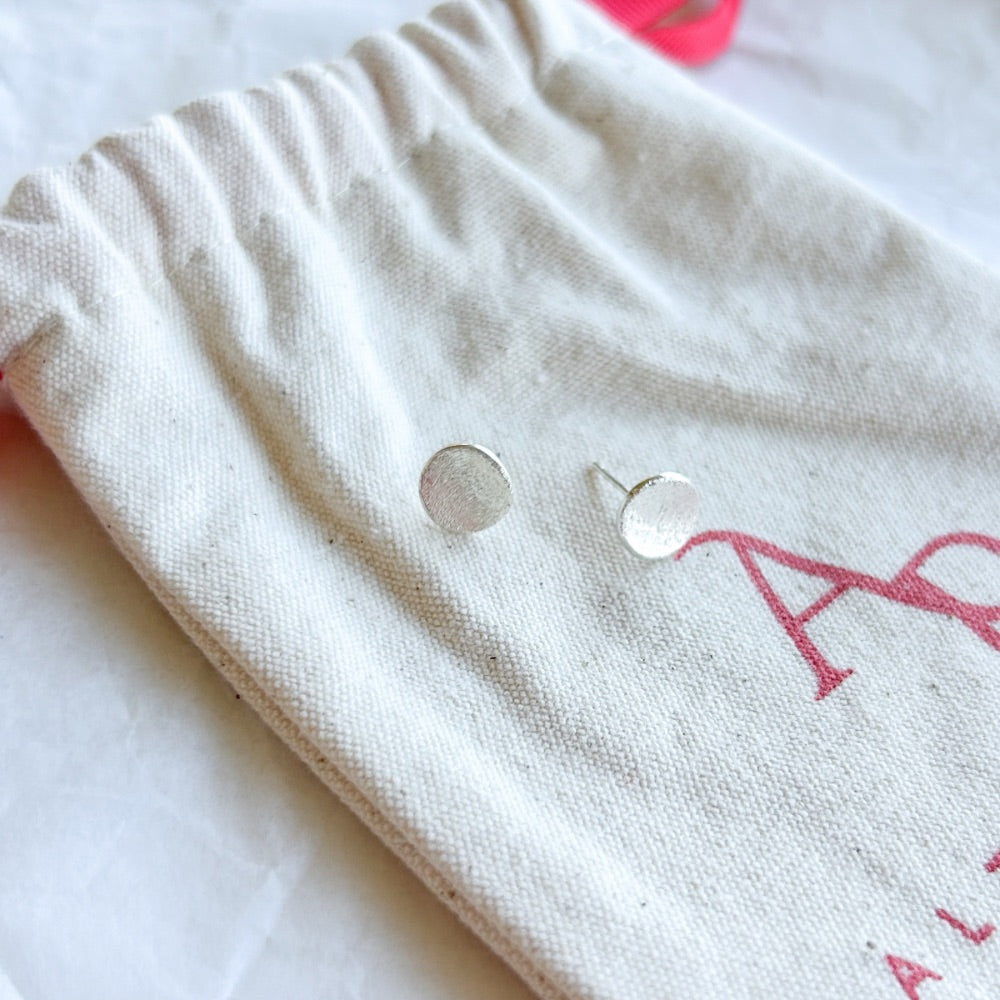 Aros de Plata Salzburgo con diseño circular texturizado, exhibidos sobre una bolsa de tela clara con lazo rojo.