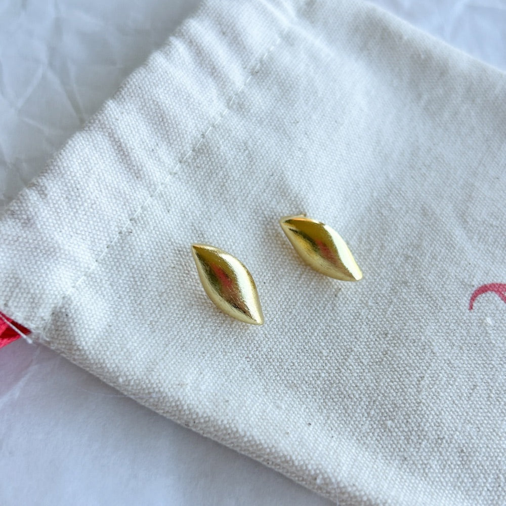 Aros Dorados Galway con diseño alargado y acabado satinado, exhibidos sobre una bolsa de tela clara con detalles en rojo.