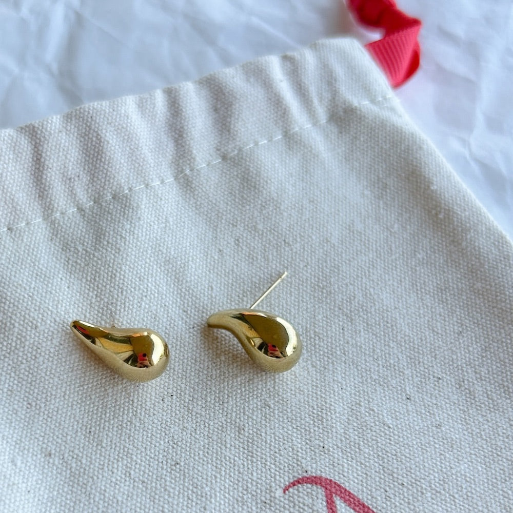 Aros Róterdam en baño de oro con forma orgánica y estilizada sobre bolsa de tela.