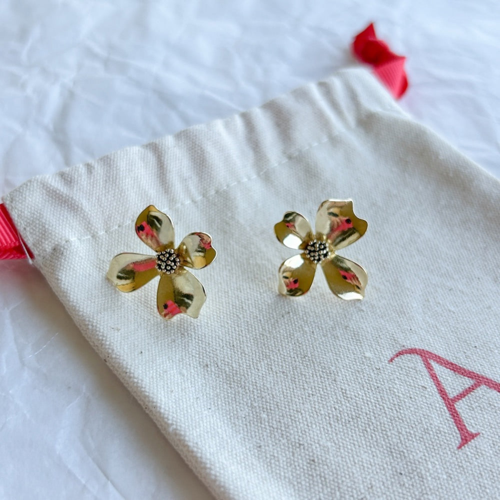 Aros Dorados Split con diseño floral brillante y centro texturizado, exhibidos sobre una bolsa de tela clara con lazo rojo.