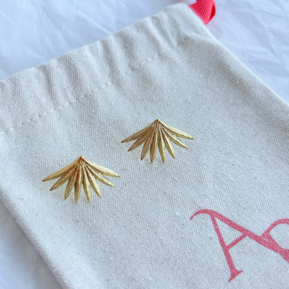 Aros Valencia en baño de oro con textura elegante sobre bolsa de tela.