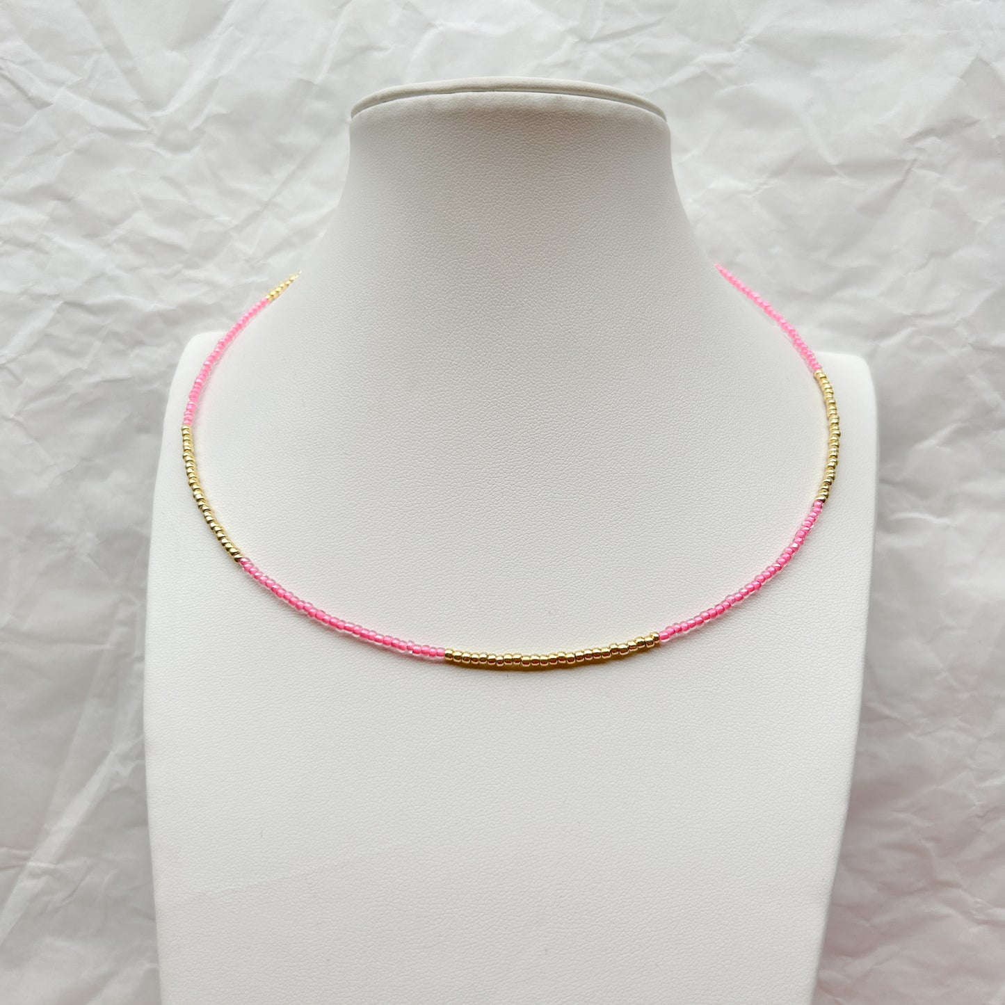 Collar Artesanal Gota con mostacillas en tonos rosa y dorado, exhibido sobre un busto blanco.