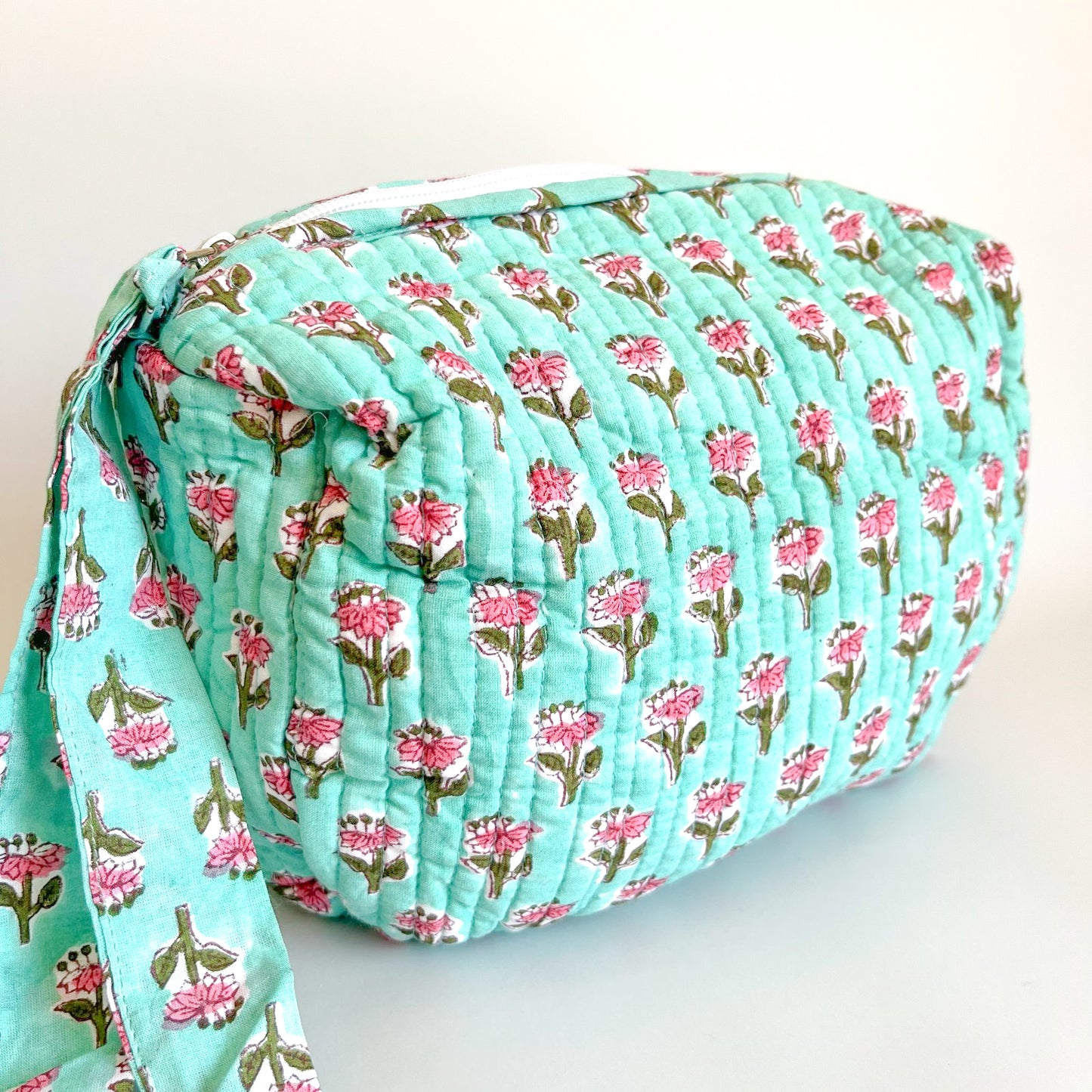Estuche acolchado con estampado de flores rosadas sobre fondo verde menta, ideal para organizar cosméticos y accesorios con estilo.