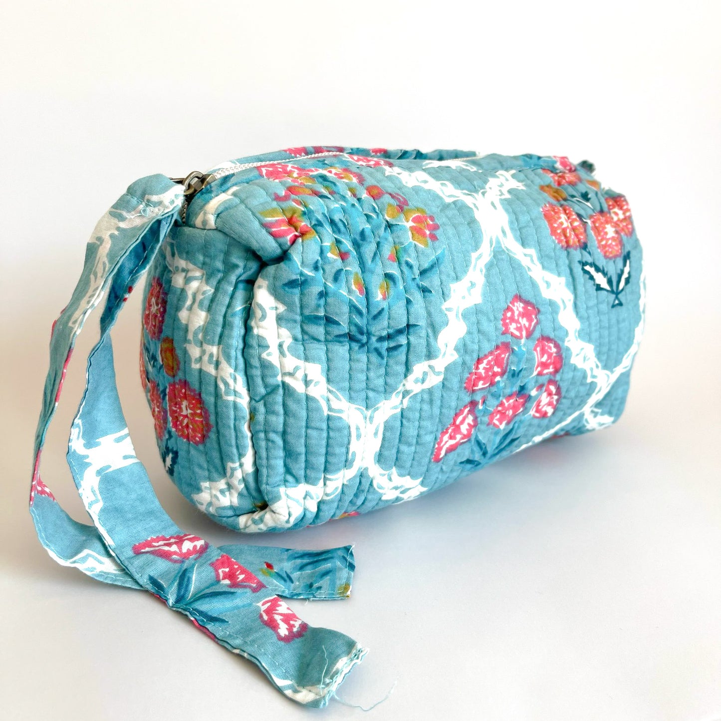 Estuche acolchado con estampado floral en tonos celestes, rojos y blancos, con cierre seguro y borla decorativa. Ideal para organizar cosméticos y accesorios con un diseño sofisticado y funcional.