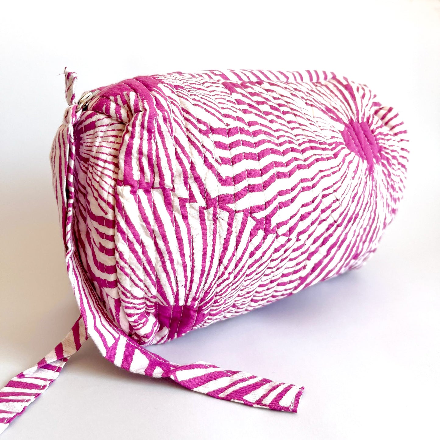 Estuche acolchado con diseño geométrico en tonos magenta y blanco, perfecto para organizar cosméticos y accesorios con un toque moderno.