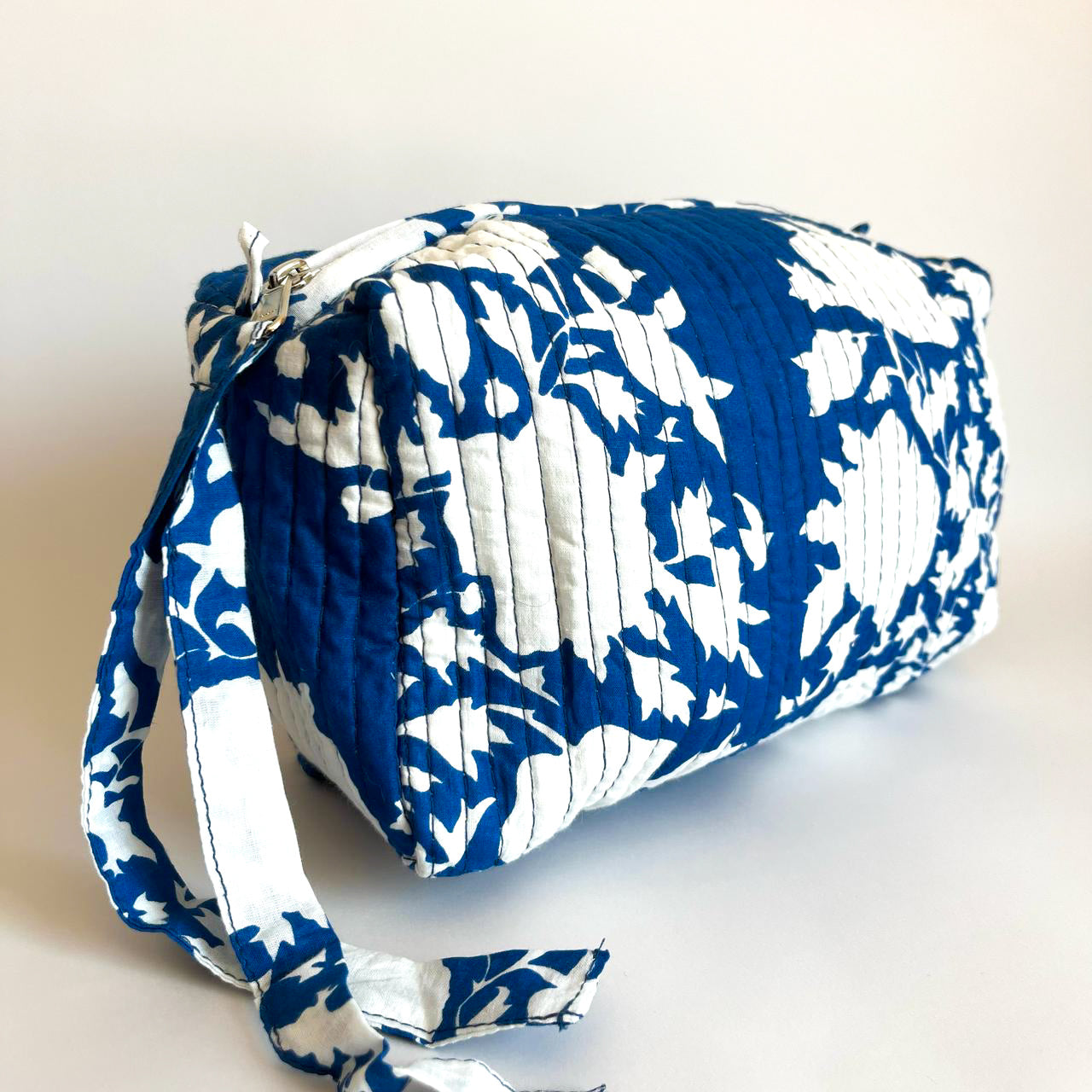 Estuche acolchado en tonos azul y blanco con diseño floral, ideal para organizar cosméticos y accesorios con estilo.
