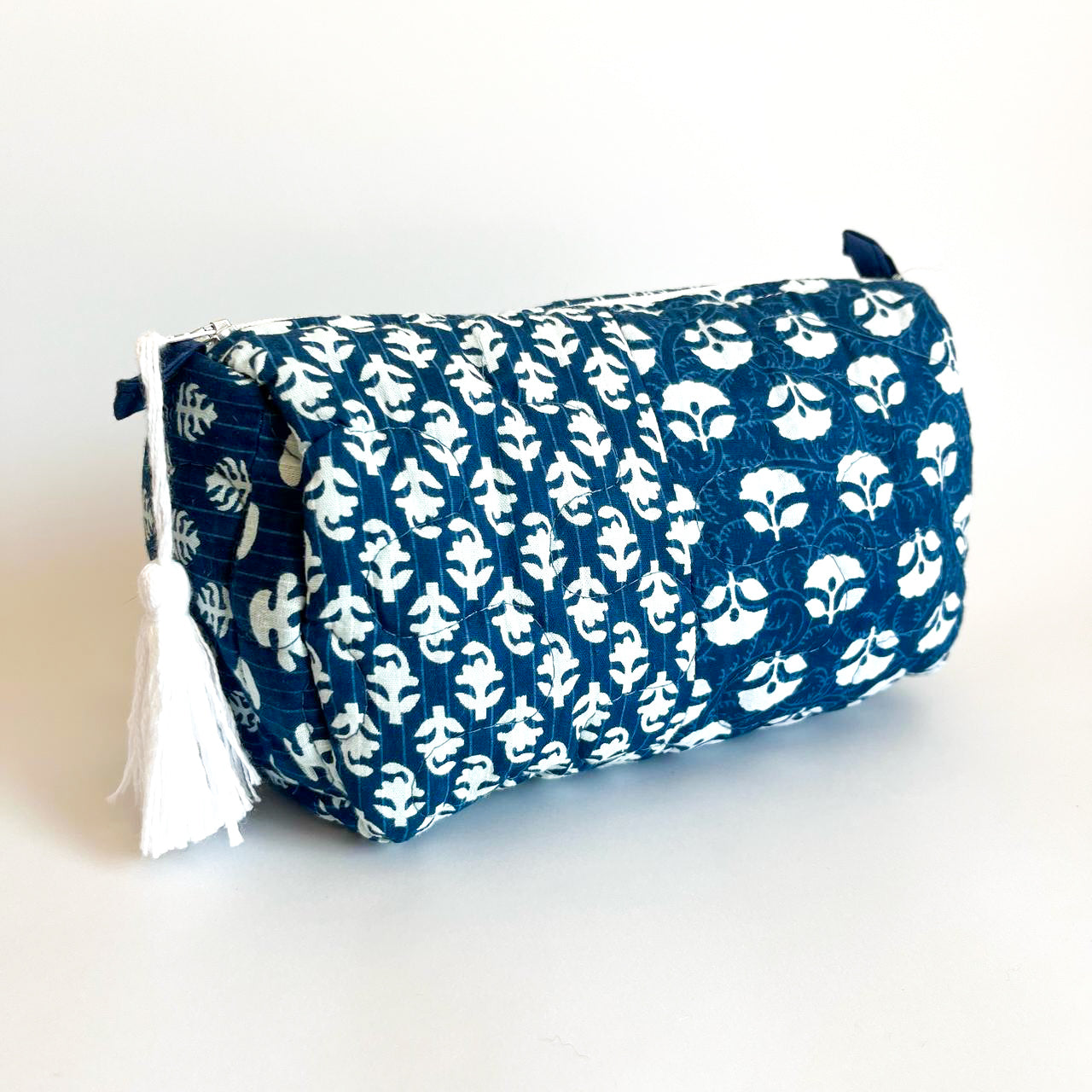Estuche acolchado en tonos azul y blanco con estampado floral y cierre superior con borla decorativa. Ideal para organizar cosméticos y accesorios con estilo.