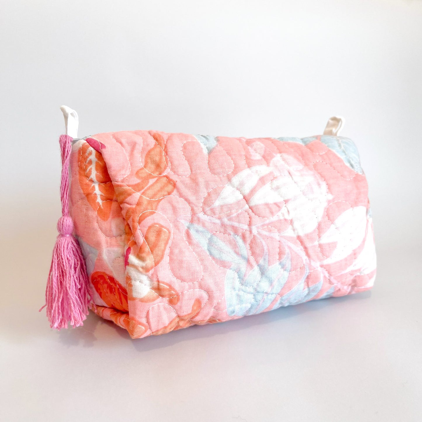 Estuche acolchado con estampado floral en tonos rosa, blanco y celeste, con borla decorativa en el cierre.