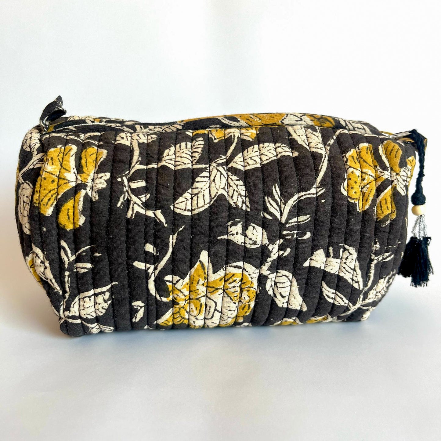 Estuche acolchado con estampado floral en negro, amarillo y blanco, con borla decorativa negra.