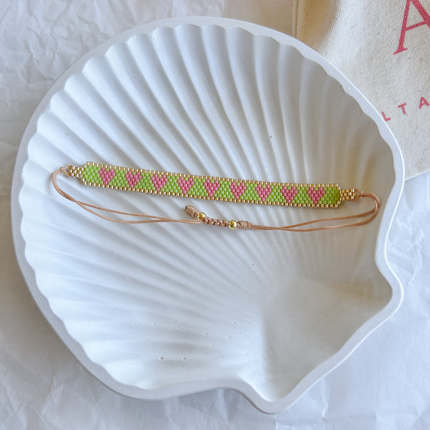 Pulsera Artesanal Corazones Josefina con corazones en verde y rosa sobre fondo dorado.