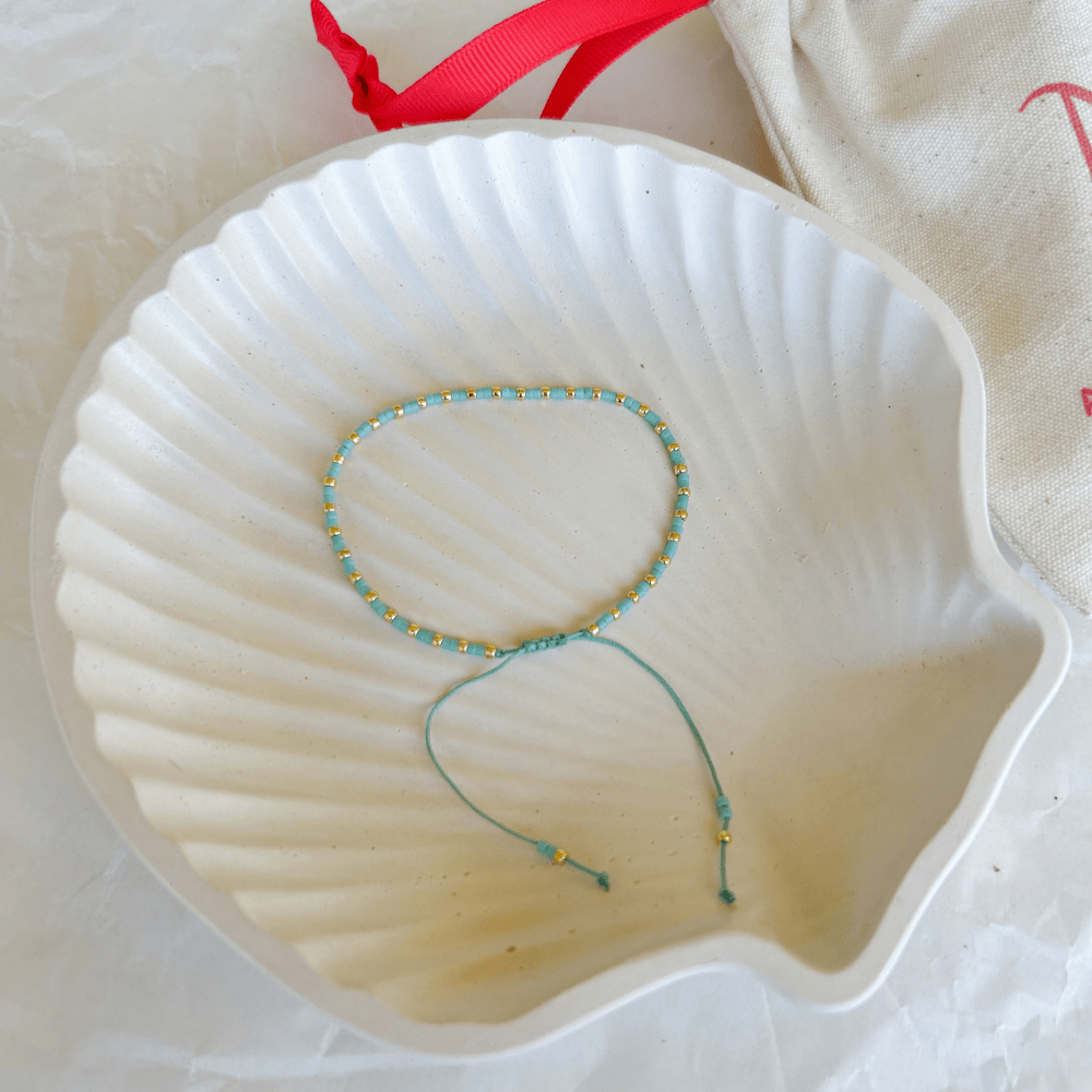 Pulsera Artesanal Simple Candelaria en color celeste sobre concha blanca.