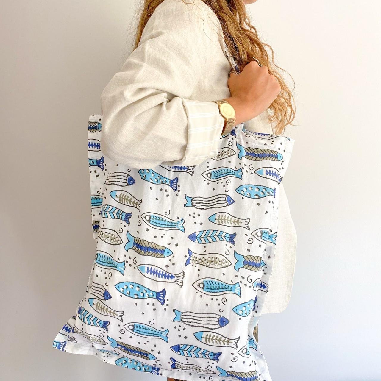 Mujer con Tote Bag Arrecife, bolsa reutilizable con estampado de peces en tonos azules y beige.