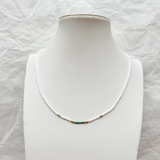Collar Artesanal Lluvia con mostacillas en tonos blanco, dorado y turquesa, exhibido sobre un busto blanco.