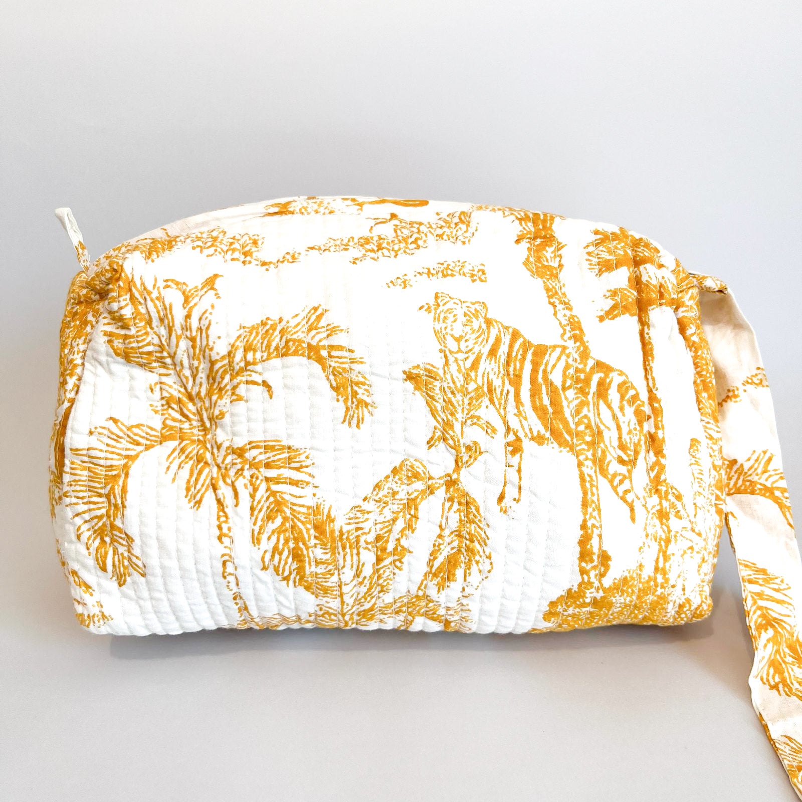 Estuche Anémona con estampado tropical en tonos dorados sobre fondo blanco.