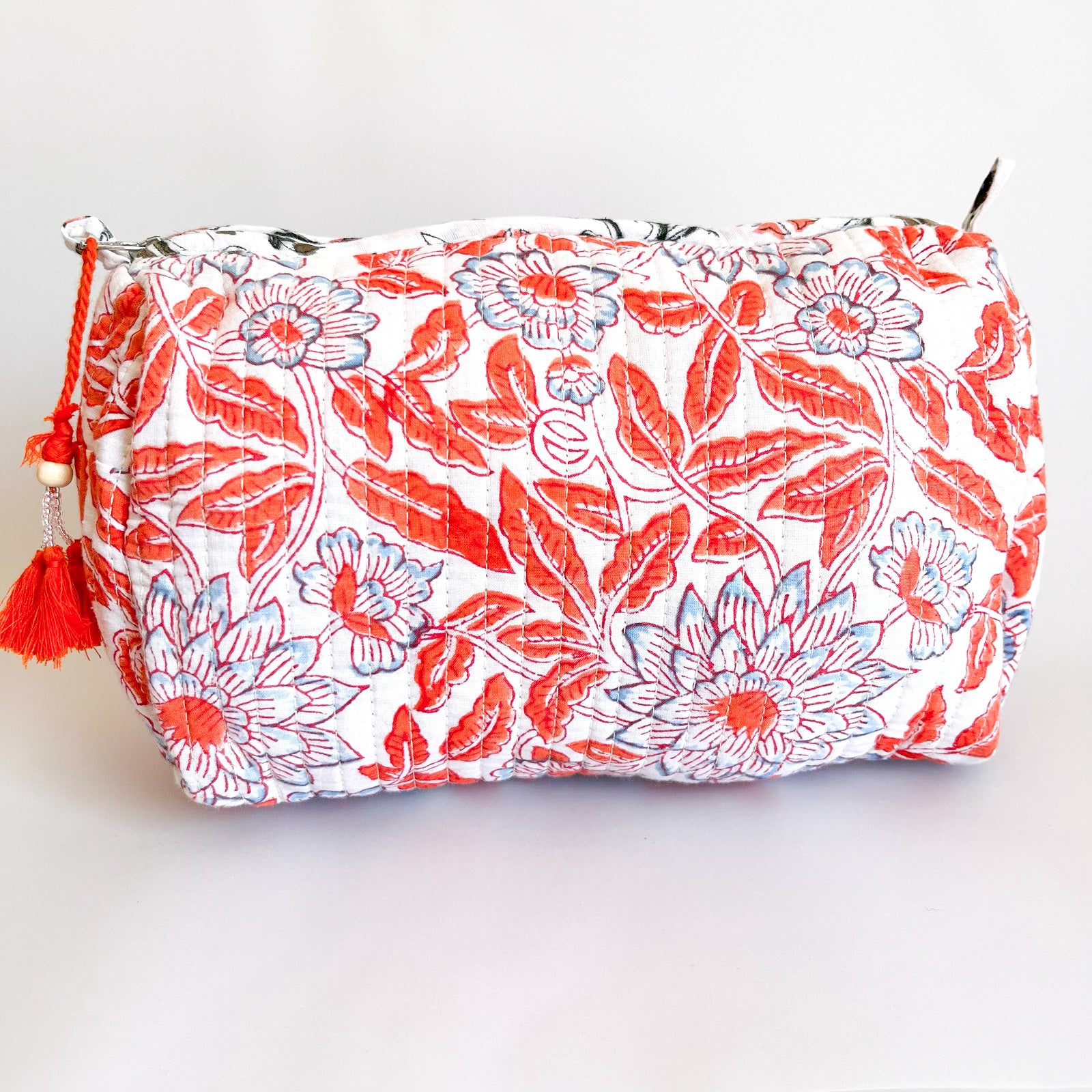 Estuche acolchado con estampado floral en tonos naranjas y azul sobre fondo blanco, con borla decorativa en el cierre.