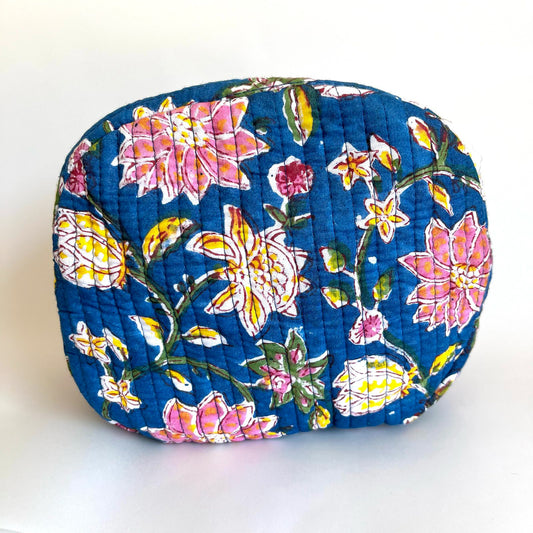 Estuche acolchado con estampado floral en tonos rosados y amarillos sobre fondo azul oscuro, con borla decorativa en el cierre.
