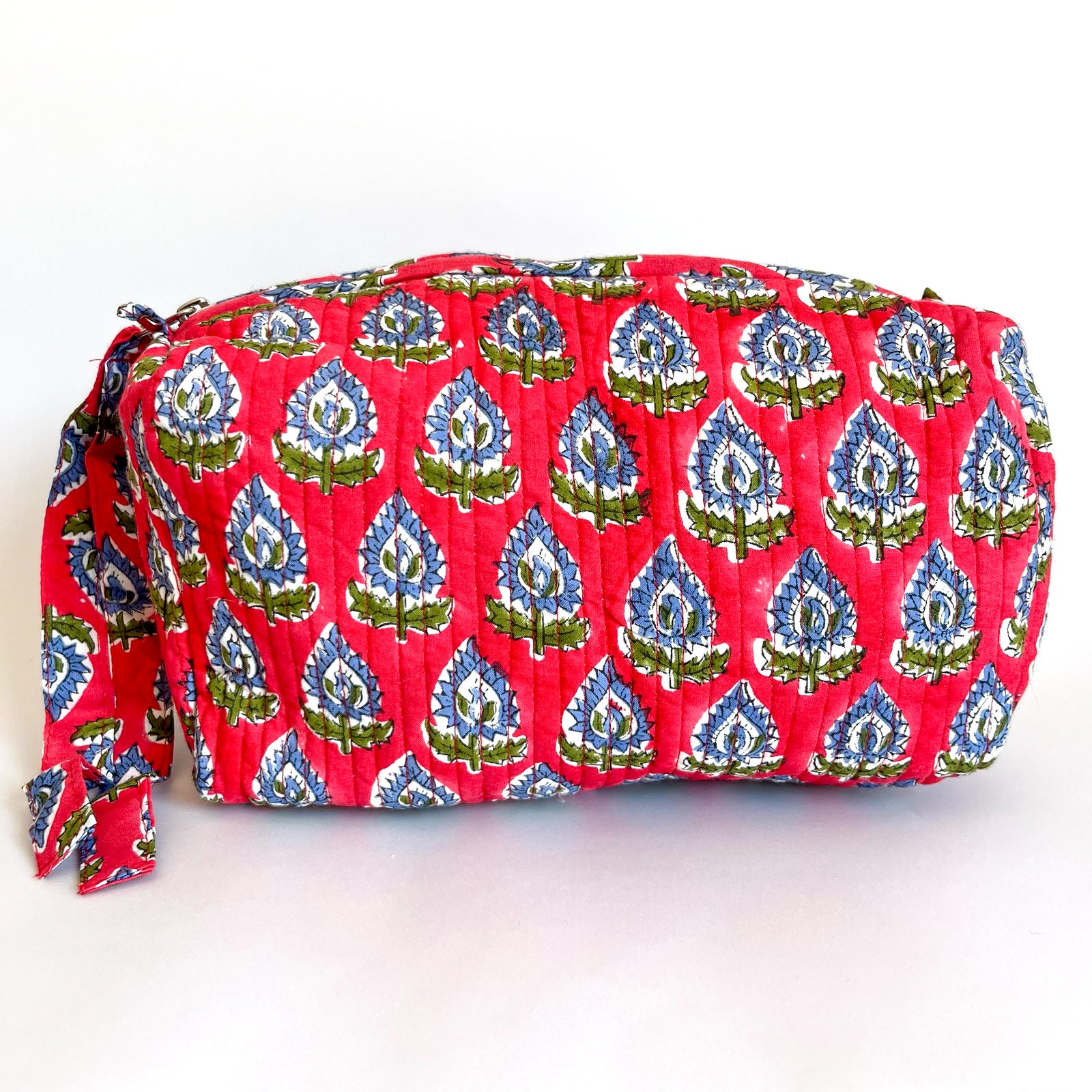 Estuche acolchado en tonos rojos y azules con estampado botánico y cierre con borla decorativa.
