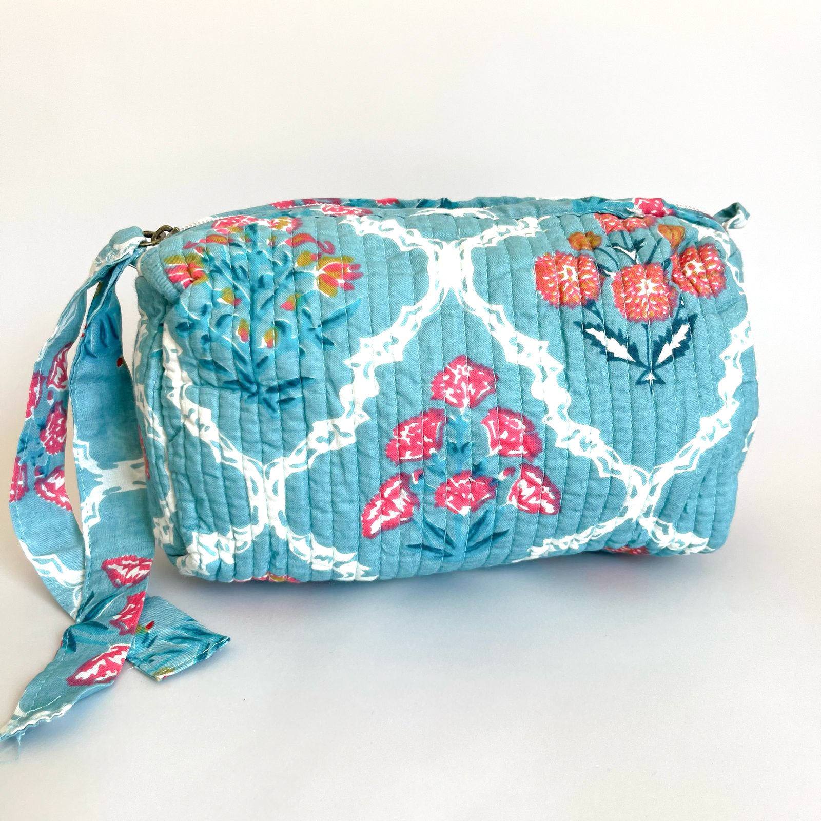 Estuche acolchado con estampado floral en tonos celestes, rojos y blancos, con cierre seguro y borla decorativa. Ideal para organizar cosméticos y accesorios con un diseño sofisticado y funcional.