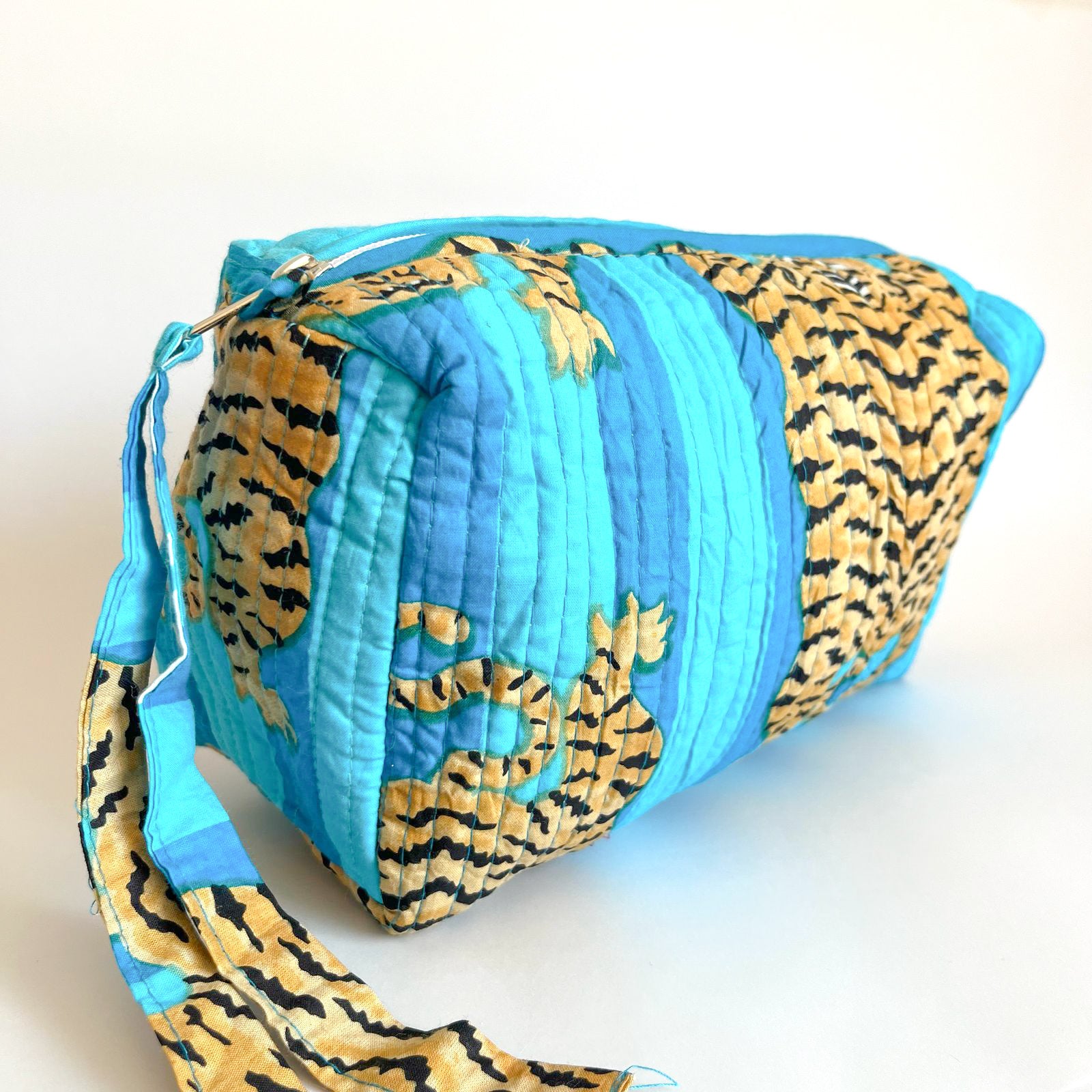 Estuche acolchado con estampado de tigres dorados sobre fondo azul vibrante, ideal para organizar cosméticos y accesorios con un diseño exótico y sofisticado.