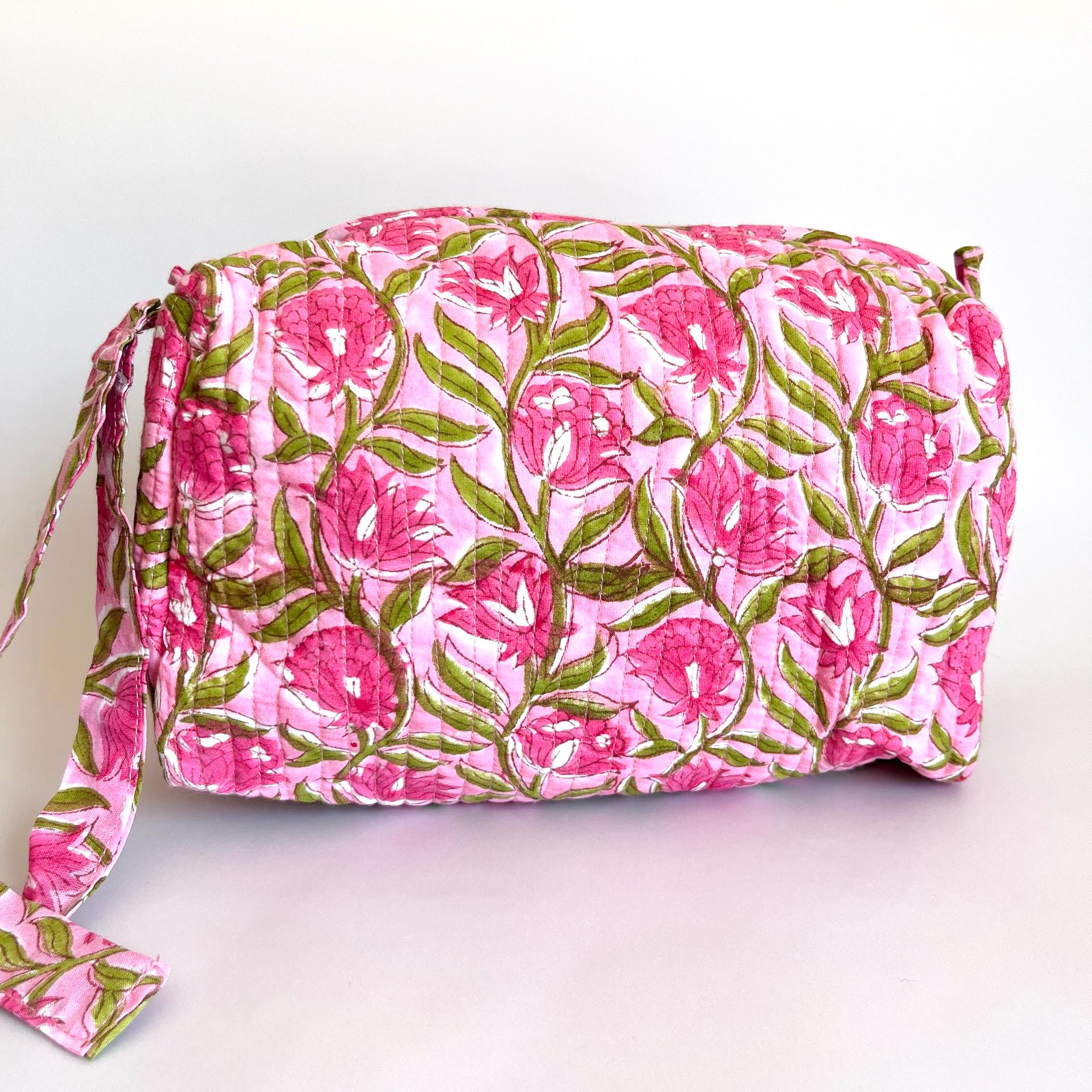 Estuche acolchado con estampado floral en tonos rosa y verde sobre fondo claro, con cierre superior y borla decorativa.
