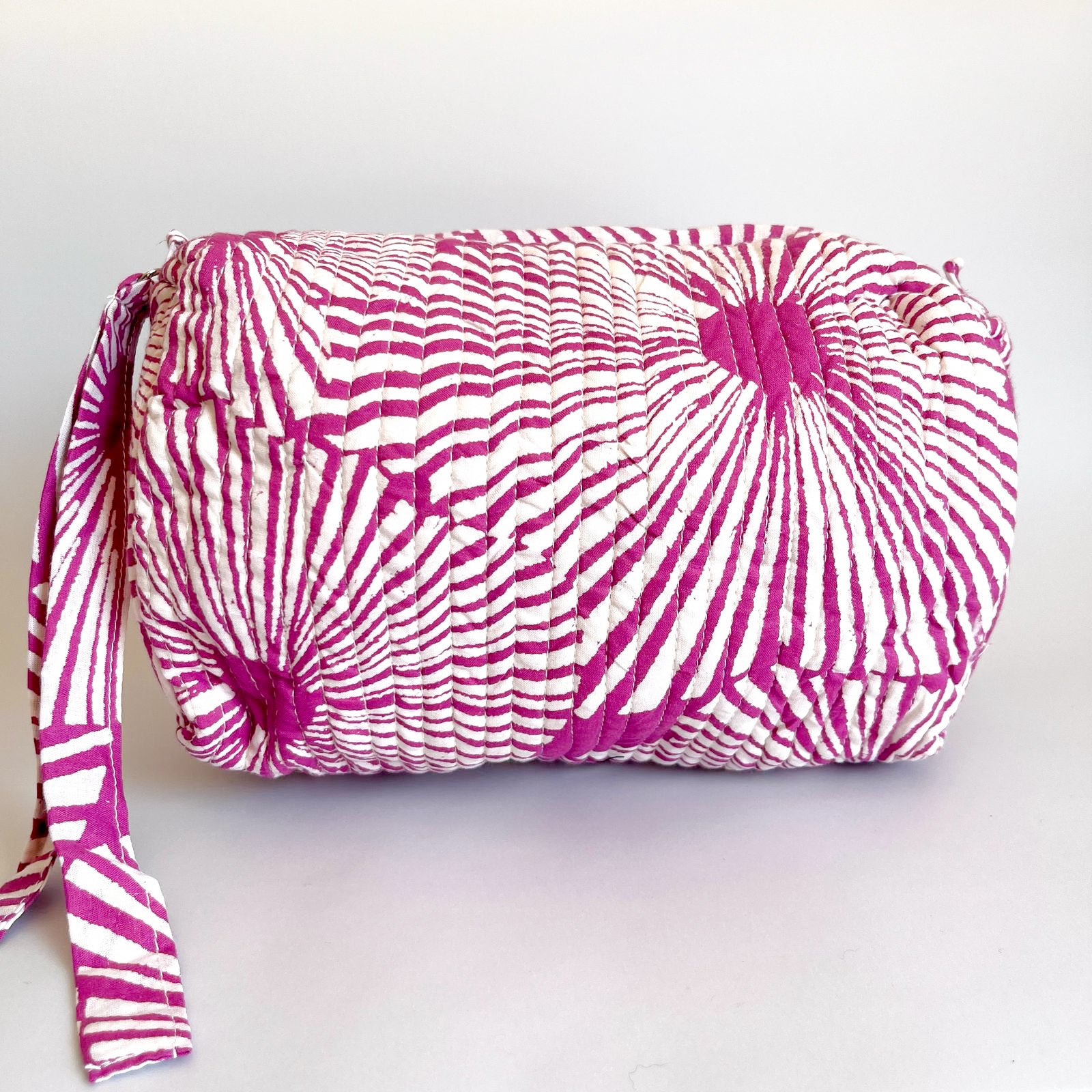 Estuche acolchado con diseño geométrico en tonos magenta y blanco, perfecto para organizar cosméticos y accesorios con un toque moderno.