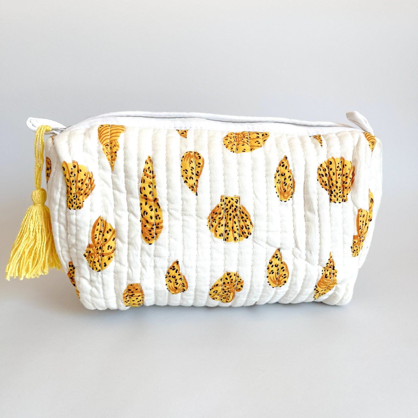 Estuche acolchado en algodón con estampado de hojas doradas sobre fondo blanco, con borla decorativa en el cierre.