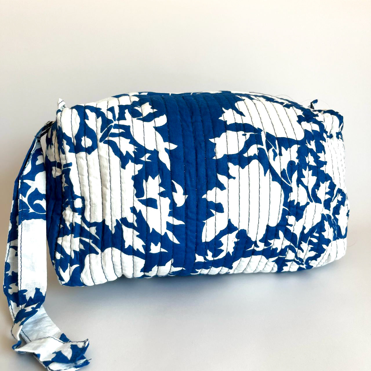 Estuche acolchado en tonos azul y blanco con diseño floral, ideal para organizar cosméticos y accesorios con estilo.
