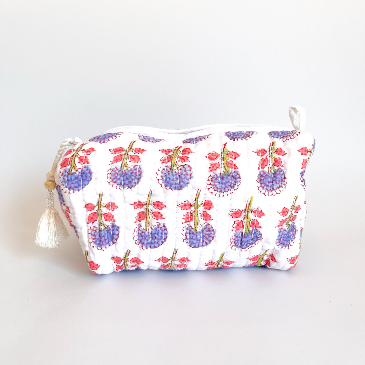 Estuche acolchado con estampado floral en tonos morados y rosados sobre fondo blanco, con borla decorativa en el cierre.