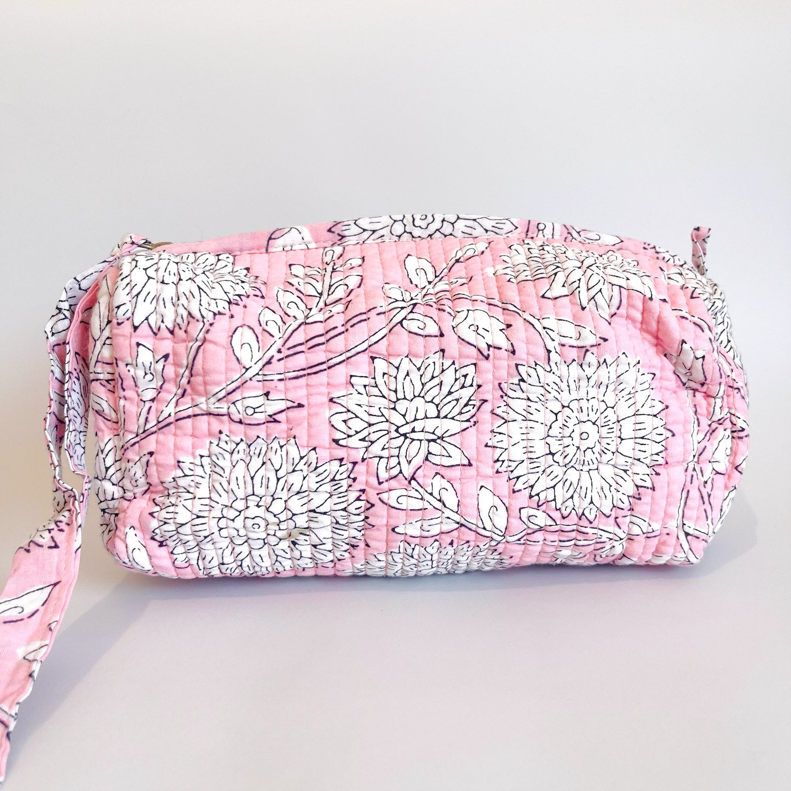 Estuche acolchado con estampado floral en tonos rosados y blancos, con borla decorativa rosa en el cierre.