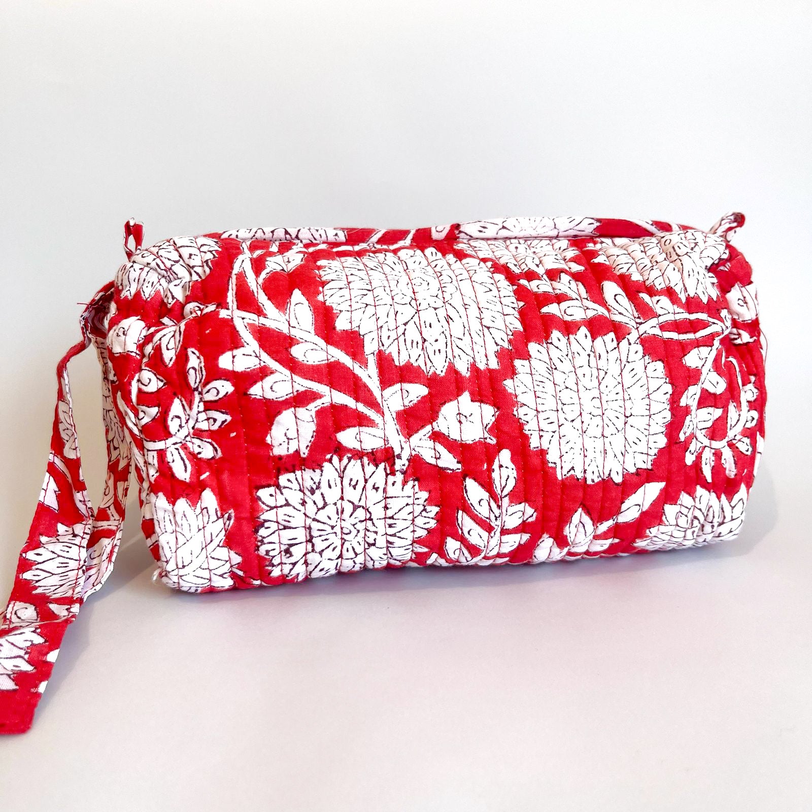 Estuche acolchado con estampado floral en tonos rojos y blancos, con borla decorativa en el cierre.