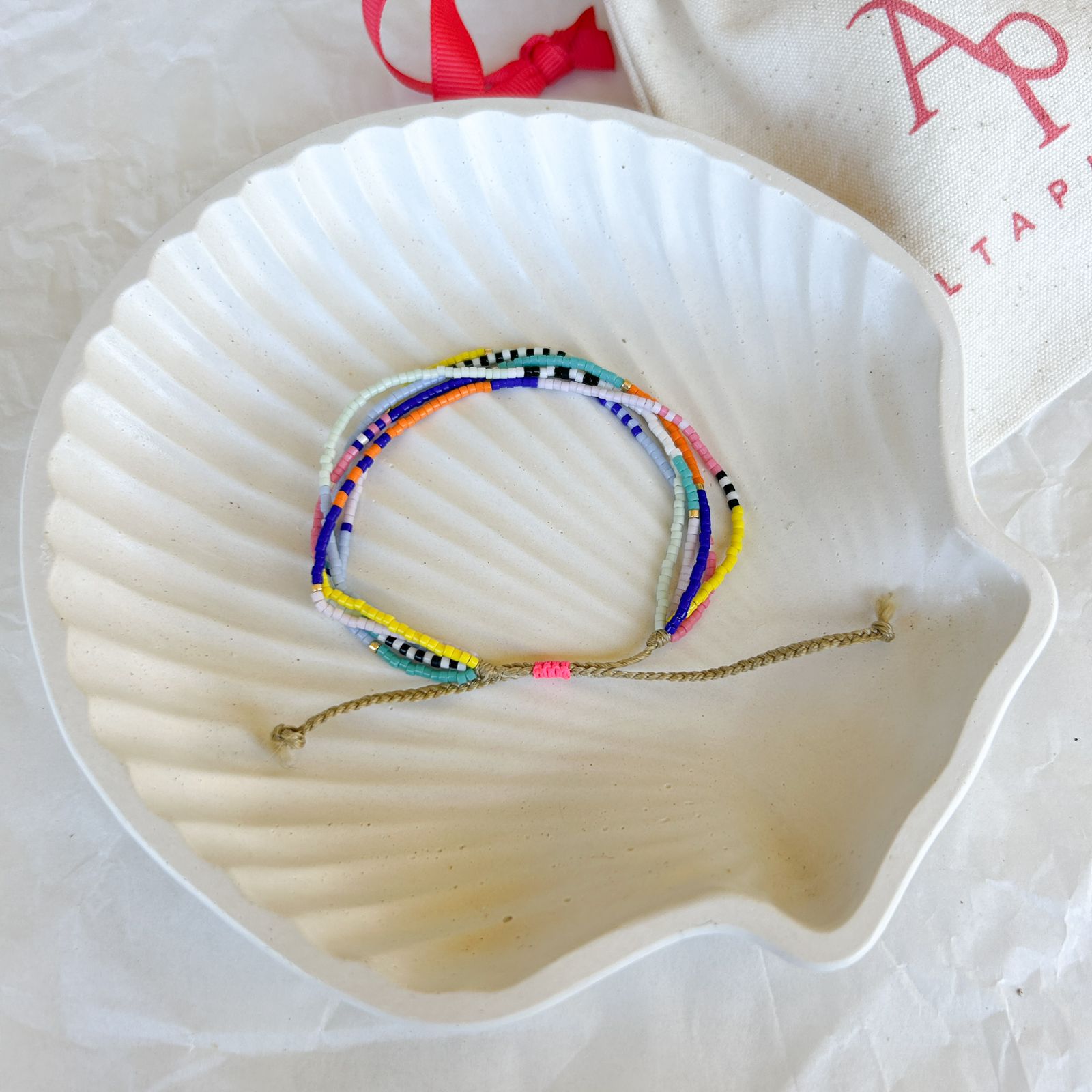 Pulsera Artesanal 5 Vueltas Juanita sobre concha blanca, mostrando cinco vueltas de mostacillas en colores vibrantes con cierre ajustable artesanal.