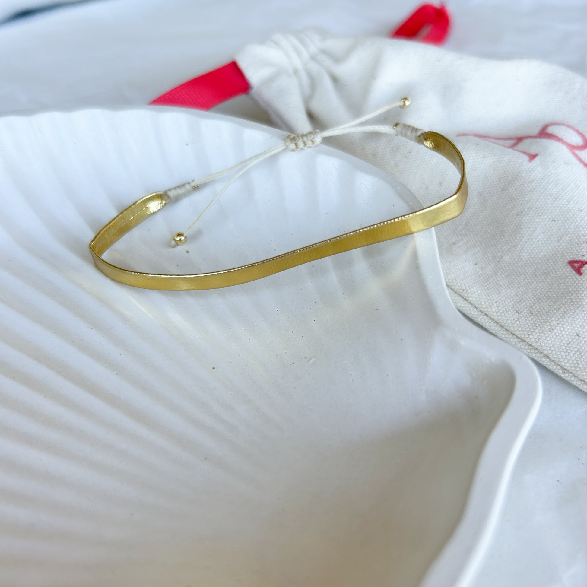 Pulsera Artesanal Cintas Colombianas Emma en tono dorado sobre concha blanca, resaltando su diseño minimalista y brillante.