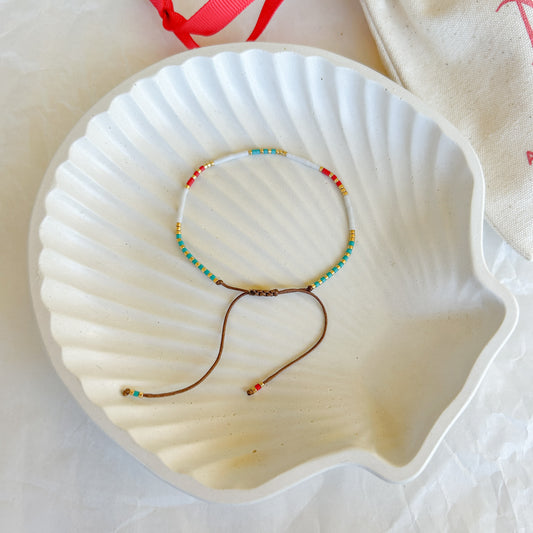 Pulsera artesanal simple Alicia con cuentas de colores vibrantes y cierre ajustable, presentada en un plato de concha blanca.
